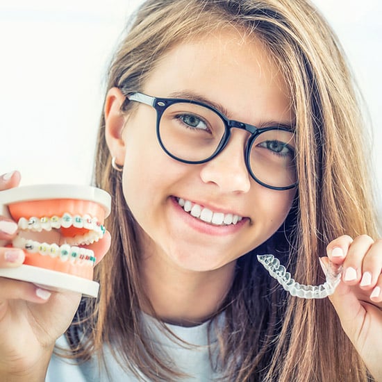 girl with model of braces and an Invisalign tray