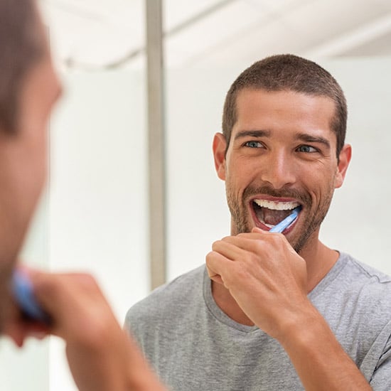 man brushing his teeth and looking in mirror