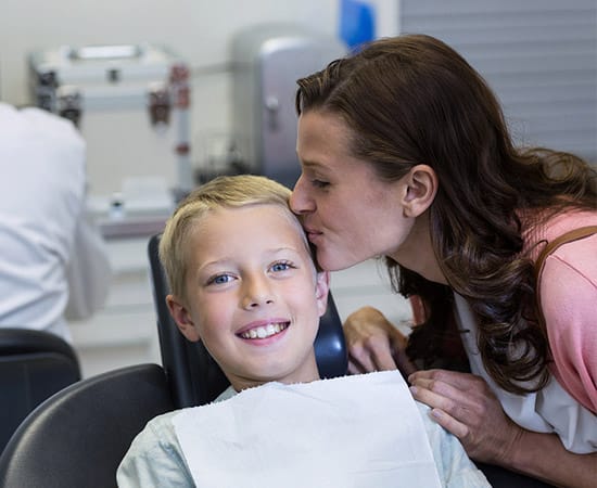 woman kissing her young son on forehead at the dentist